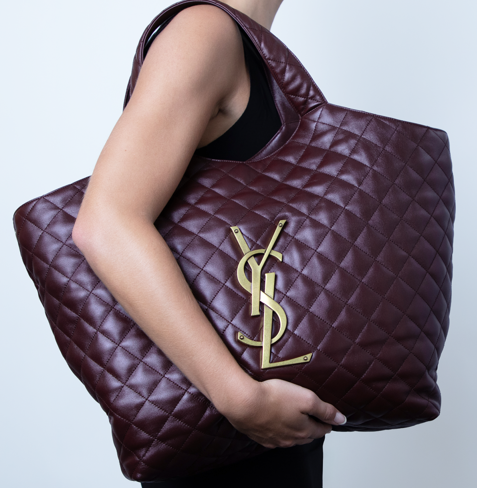 Woman holding a large dark purple YSL handbag over her shoulder