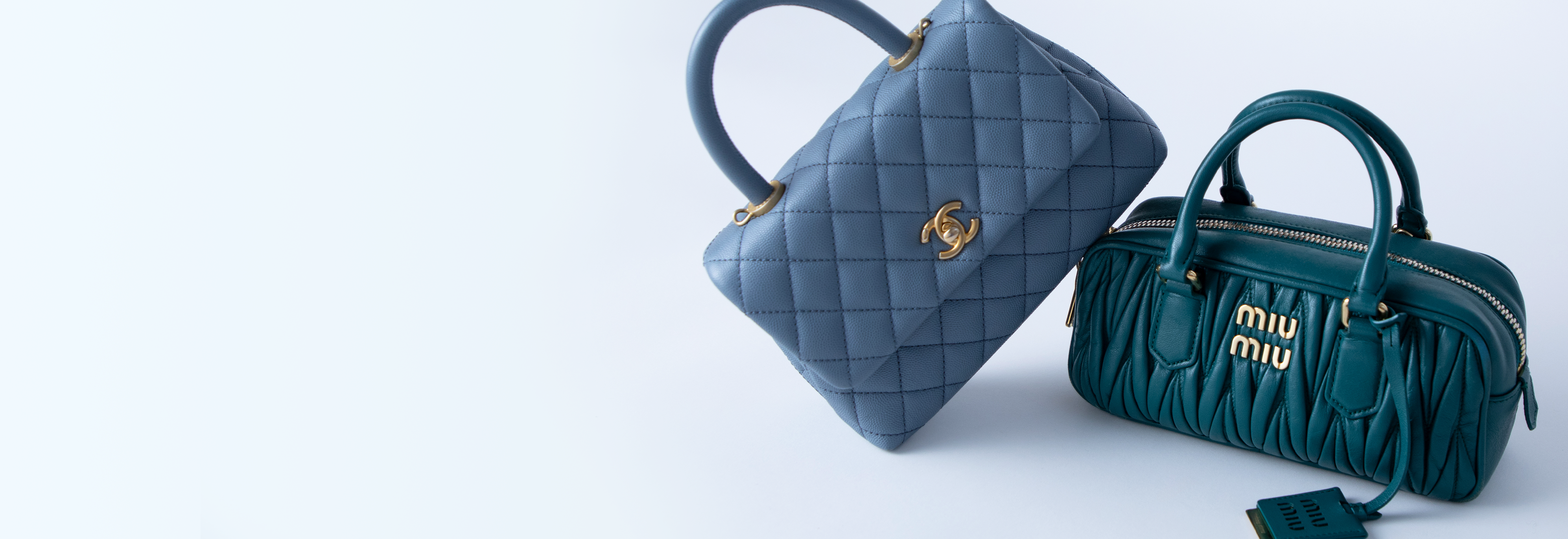 Light blue Chanel handbag leaning against a teal Miu Miu handbag against a sky blue background